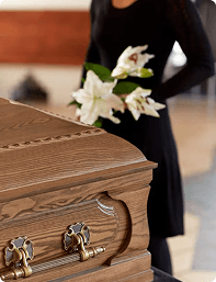 Mourner placing white lilies on a wooden casket