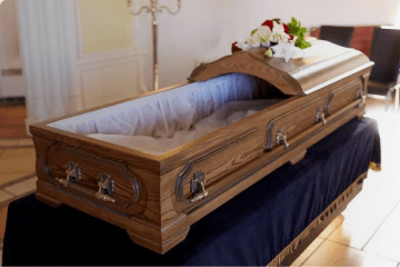 Open wooden casket with white lining on a navy draped stand