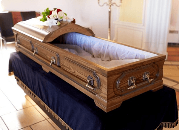 Open wooden casket with white satin lining on a navy draped stand